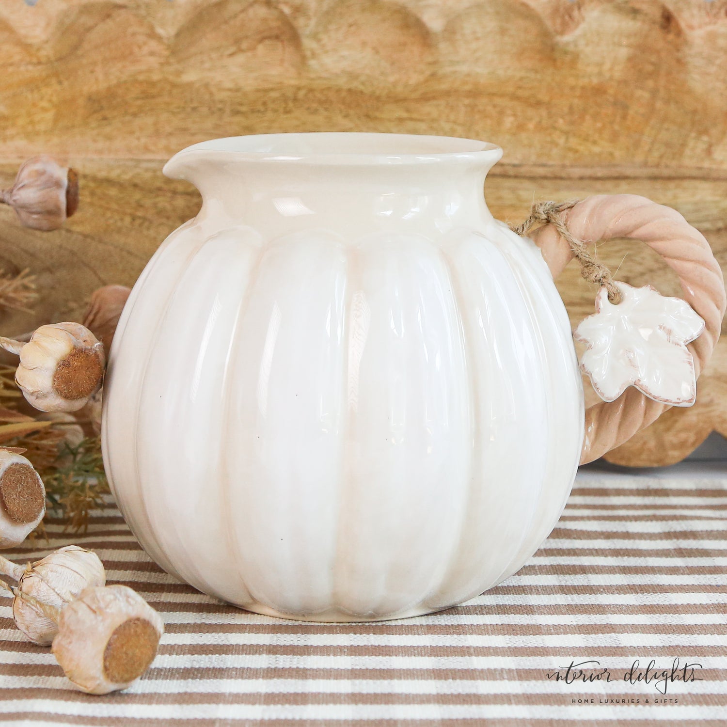 Functional ceramic white pumpkin pitcher ideal for serving drinks, showcased with mixed green foliage.