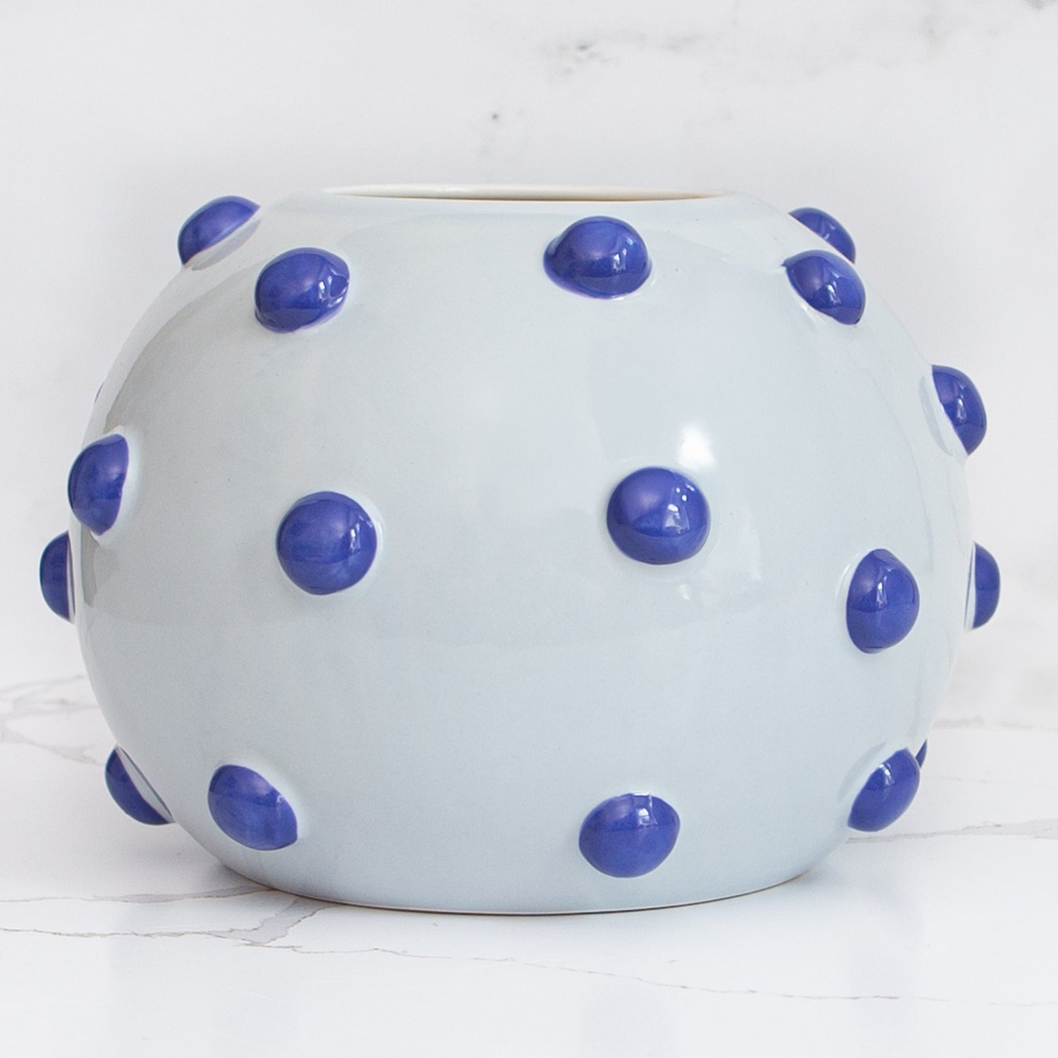 The 10” Luxe Round Ceramic Vase with Blue Knobs, showcasing its 10.5" diameter and 7" height in a cozy living space.