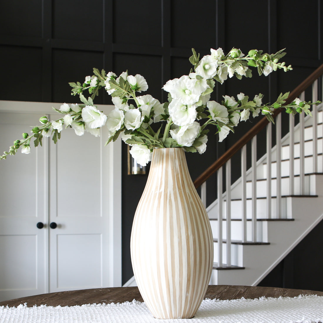 Hollyhock &amp; Large Striped Vase Arrangement showcasing a stunning 21-inch tall natural striped vase filled with vibrant 43-inch tall hollyhock stems.