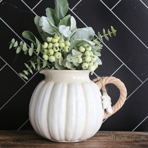 Charming white pumpkin pitcher with a twisted vine handle and leaf accent tag, perfect for fall decorating.